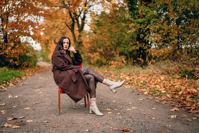 Young beautiful woman with old armchair on the country lane in autumn