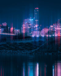 Illuminated buildings by river against sky at night