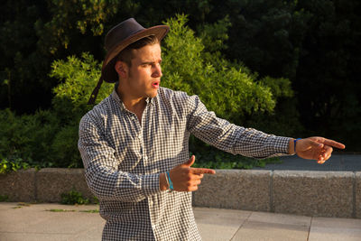 Young man wearing hat and checks shirt looking away while standing on street