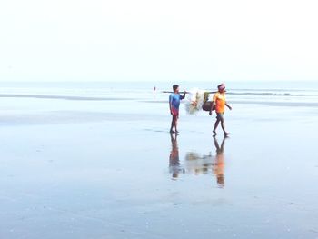 Men walking on beach against clear sky