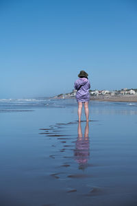 Rear view of woman standing at beach against clear blue sky