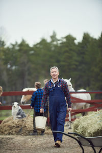 Farmer carrying bucket and pitchfork while walking in farm