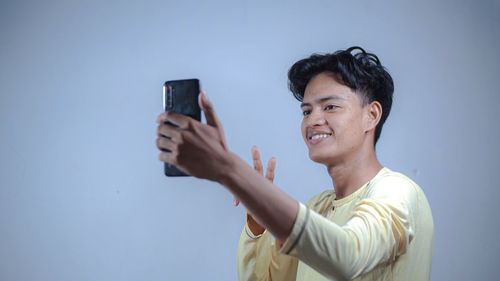 Portrait of smiling young man using mobile phone against clear sky