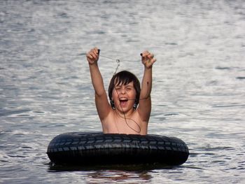 Cheerful shirtless boy with headphones and inflatable ring swimming in sea