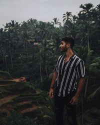 Young man looking away against trees in forest