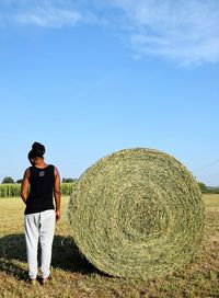 Rear view of woman standing by hay bale on field against sky