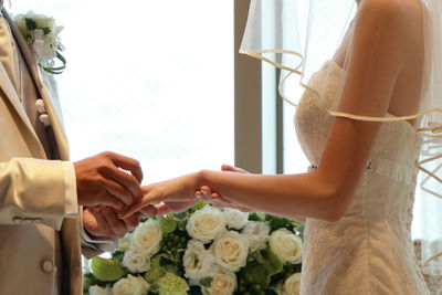 Midsection of bridegroom putting ring on bride finger during wedding ceremony