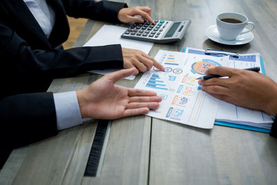 Midsection of business persons arguing over document on table at office