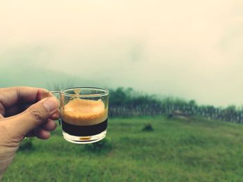 Midsection of person holding drink against sky