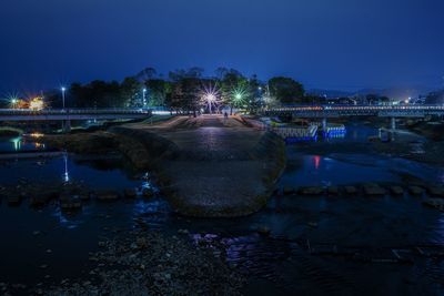 Illuminated bridge over river against sky at night