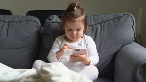 Full length of woman using mobile phone while sitting on sofa