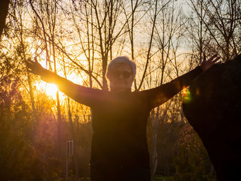 Portrait of senior woman with arms outstretched standing against sky during sunset