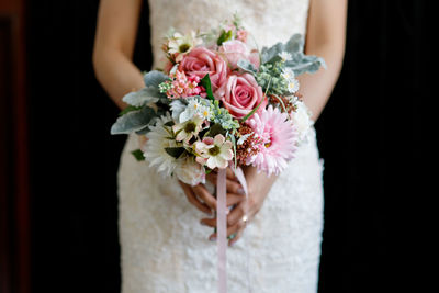 Midsection of bride holding bouquet against black background
