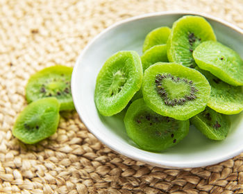Pieces of dry kiwi in a bowl on a straw mat background