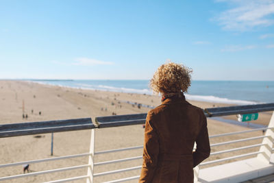 Rear view of woman standing by railing on scheveningen pier at beach against sky