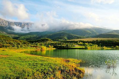 Scenic view of lake surrounded by mountains against cloudy sky