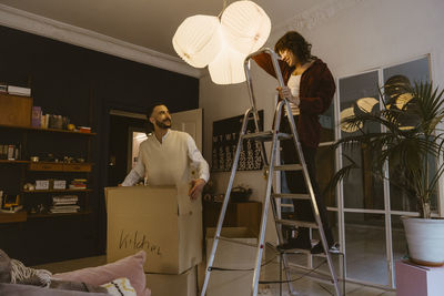 Man helping boyfriend standing on ladder during relocation