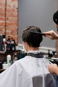 Barber in protective mask and latex glove styling adult man in a barbershop salon. new normal