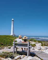 Lighthouse by sea against clear blue sky