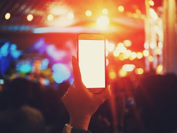 Cropped hand of woman holding mobile phone at concert