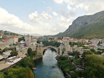 Arch bridge over river amidst buildings in city against sky