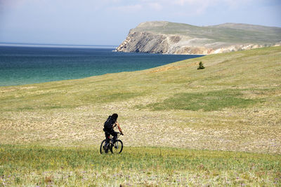 Rear view of man riding bicycle on land against sky