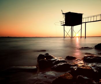 Silhouette rock on beach against sky during sunset