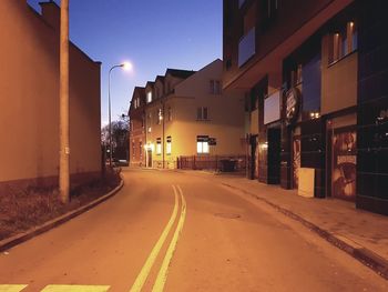 Empty road along illuminated buildings at night