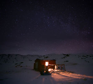 Illuminated house on snow covered landscape against star field