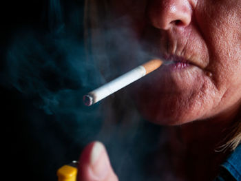 Cropped image of woman smoking cigarette against black background