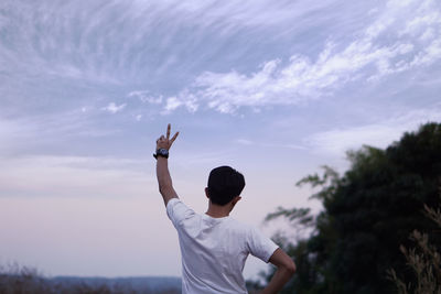 Rear view of man with arms raised standing against sky