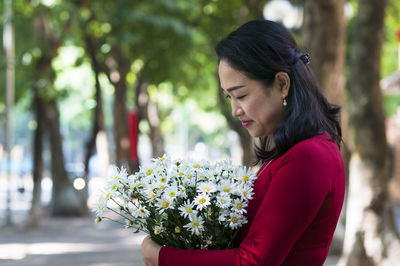 Beautiful woman standing by red flowering plant against trees