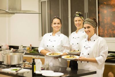 Portrait of happy female chefs holding pasta in plates while standing in commercial kitchen