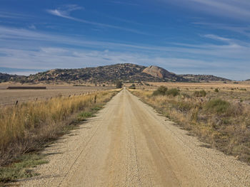 Empty dirt road amidst field
