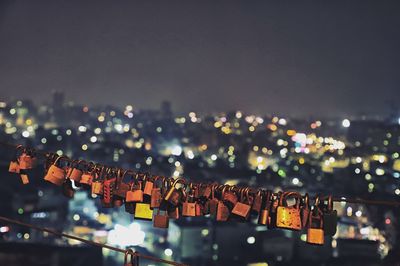 Close-up of padlocks against illuminated city against sky at night