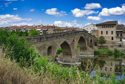 Arch bridge by buildings against sky in city