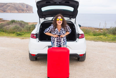 Portrait of young woman standing by car on road