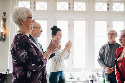 Male and female friends clapping hands while standing by table in restaurant