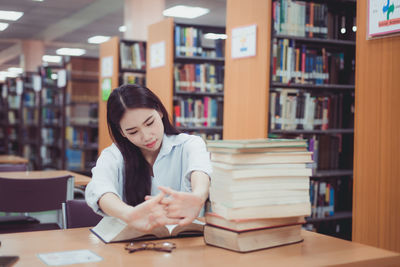 Young woman reading book while sitting on table in library