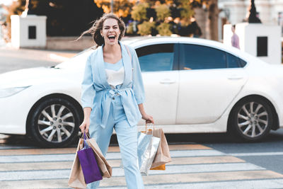 Portrait of cheerful girl with shopping bags walking on road
