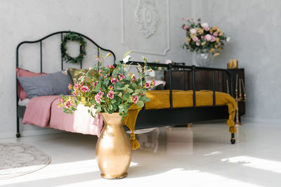 Golden vase with flowers near the bed in the bedroom