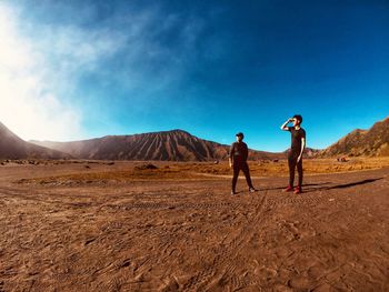 Friends standing at desert against blue sky during sunny day