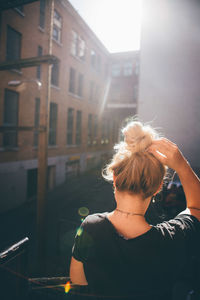 Rear view of woman with hand in hair standing by buildings in city