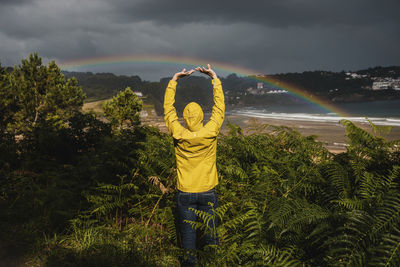 Rear view of woman with raised arms by plants during rainy season