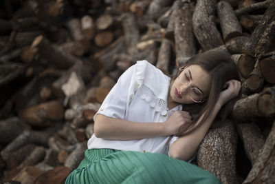 Portrait of a romantic woman with vintage clothes and glasses leaning on some wooden logs