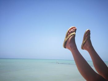 Low section of woman at beach against clear blue sky