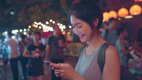 Woman using mobile phone in market at night