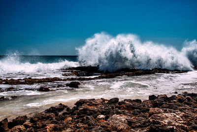 Waves breaking on rocks at beach against sky