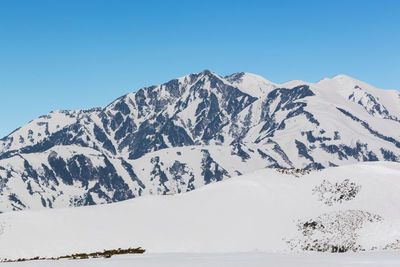 Scenic view of snow covered mountains against clear blue sky