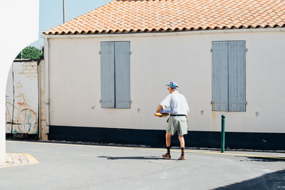 Rear view of man walking on road by house during sunny day